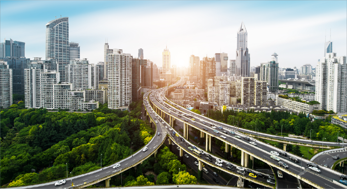 City skyline with stacked highway ramps weaving through a green, urban landscape at sunset.